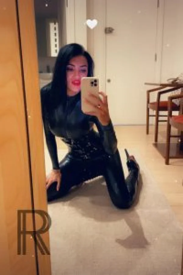 Mistress Elizabeth taking a selfie wearing a latex bodysuit