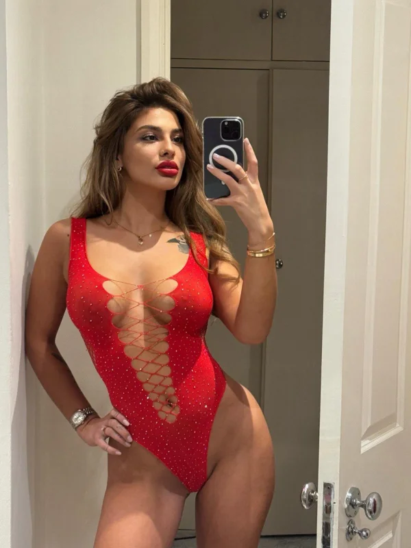 Busty lady wearing a red basque taking a picture of herself in the mirror 