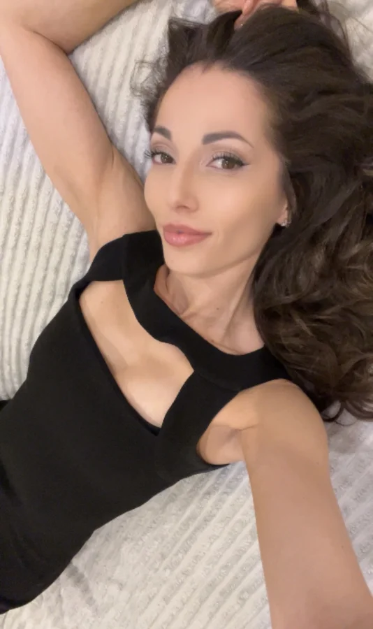 A very sexy brunette lady is spread across her bed taking this selfie picture 