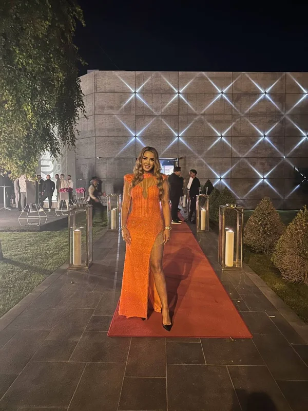 A sexy blonde escort pictured wearing a long orange dress 
