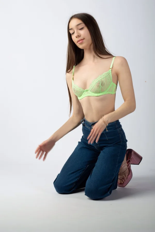 A very sexy brunette lady wearing a green bra and jeans is kneeling down 